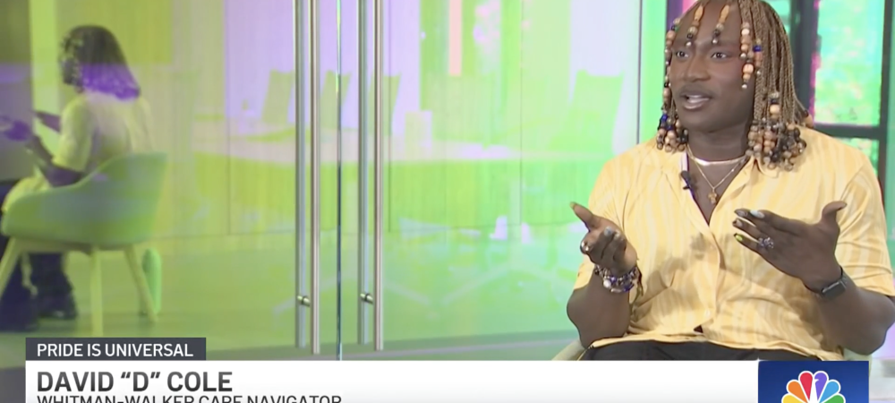 David "D" Cole, a Whitman-Walker care navigator, speaks during a televised interview; colorful glass and a seated person are visible in the background.